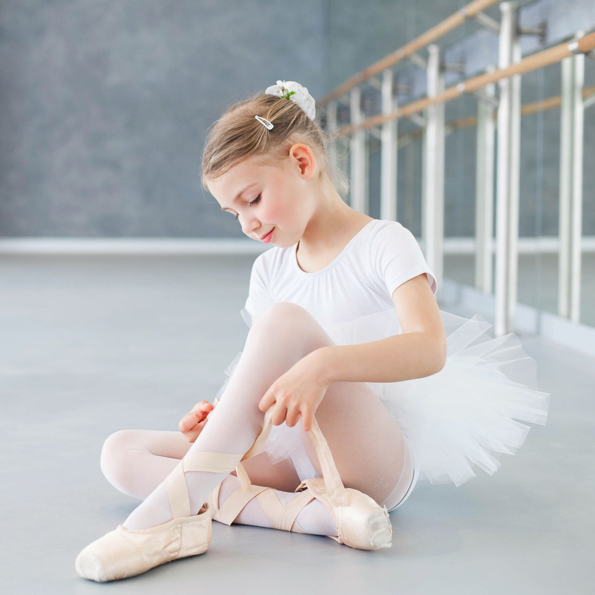 A little girl wearing pink ballet tights by Fashion Accessory Company.  The girls is sitting down and tying her pointe shoes over her pink ballet tights